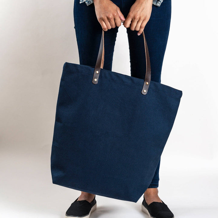Person holding a navy blue tote bag with brown handles on a plain background