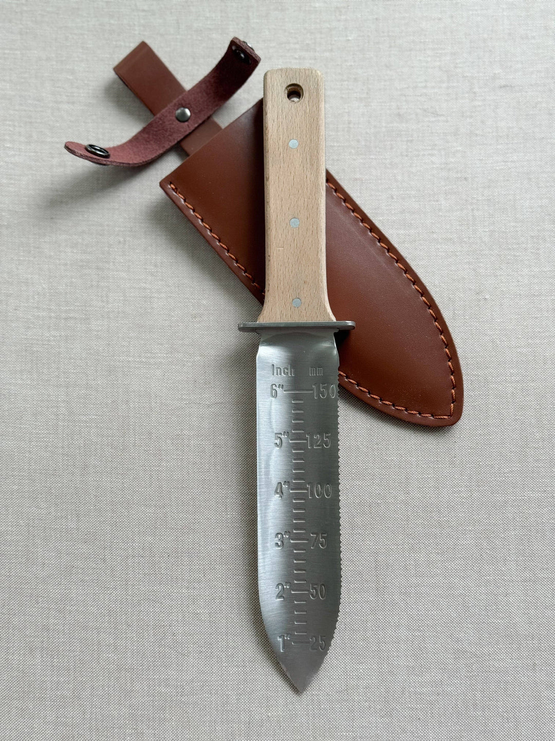 Knife with wooden handle and leather sheath on a light gray background
