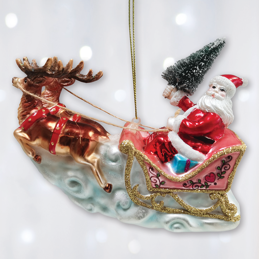 A festive Christmas ornament depicting Santa Claus in a pink sleigh pulled by a metallic bronze reindeer, with a small snowy tree on Santa's shoulder, hanging against a soft white bokeh background.