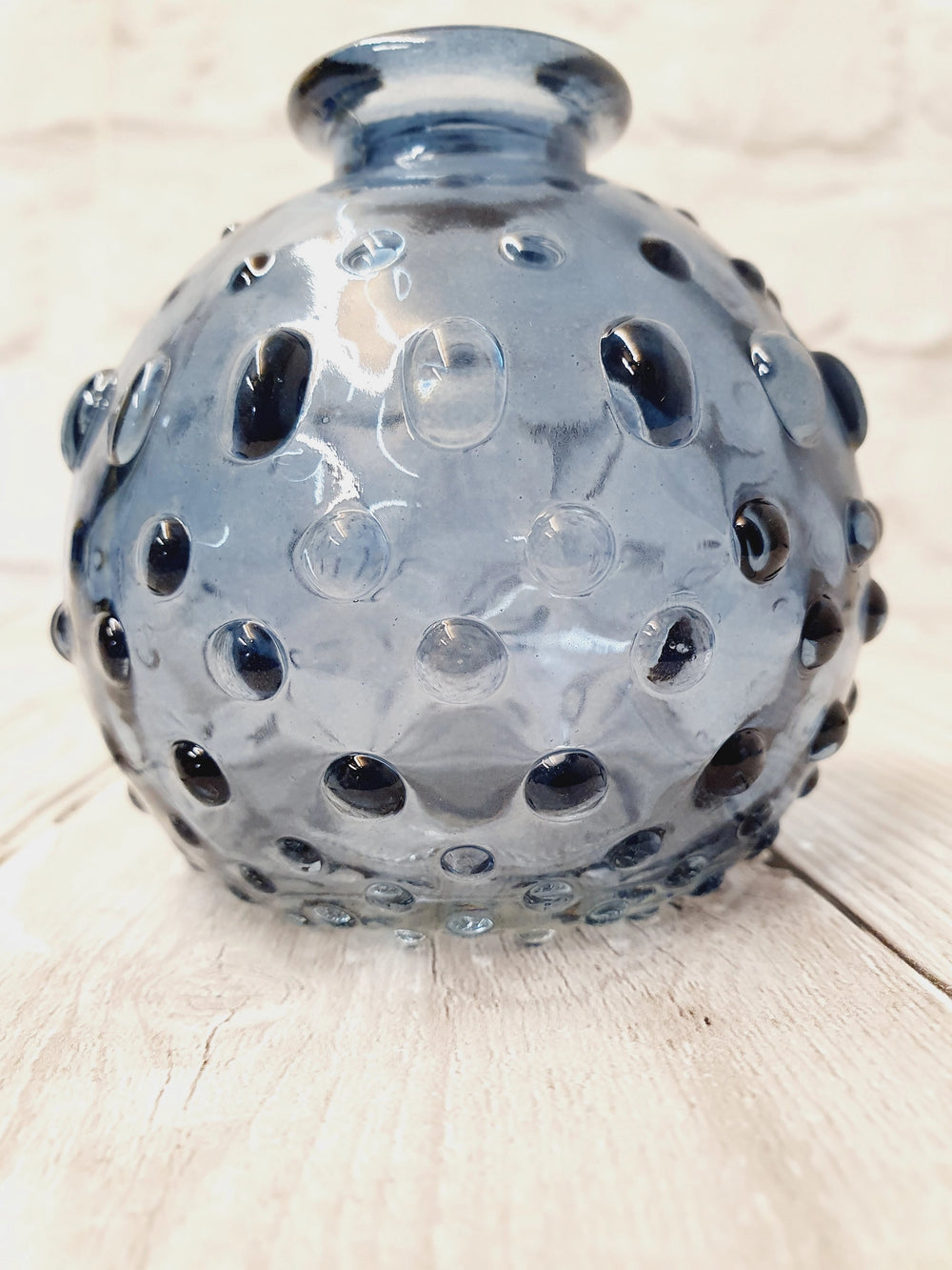Decorative glass vase with dot pattern on a light wooden surface