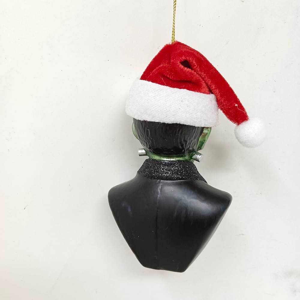 Decorative ornament of a green-skinned monster wearing a black jacket and a Santa hat on a white background
