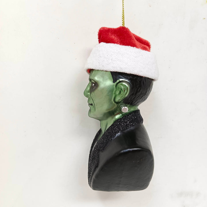 Ornament of a character with green skin, black hair, and a Santa hat on a white background