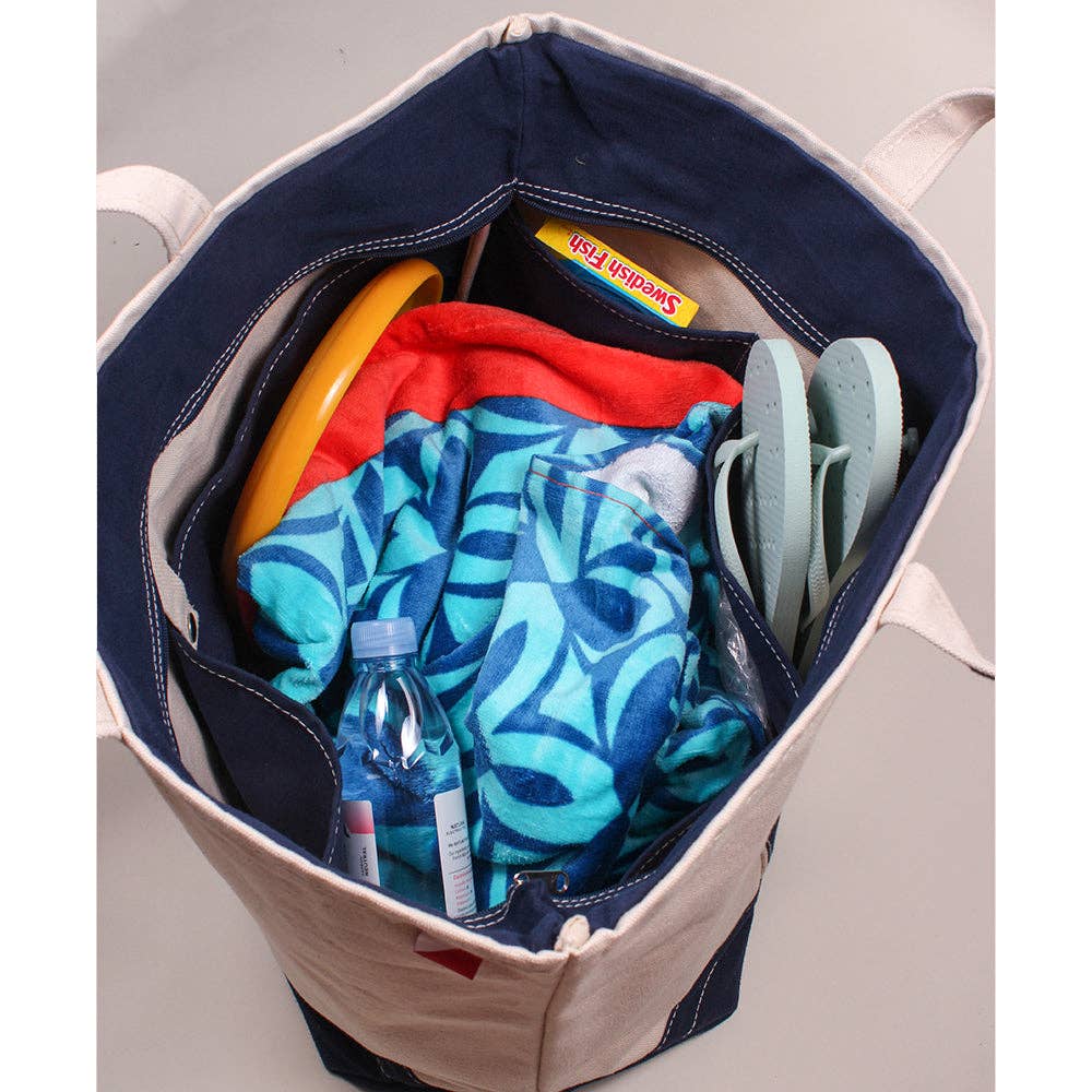 Canvas tote bag with samples of what can go inside of it including two towels, flip-flops, Swedish Fish candies, Frisbee, and a bottle of water.