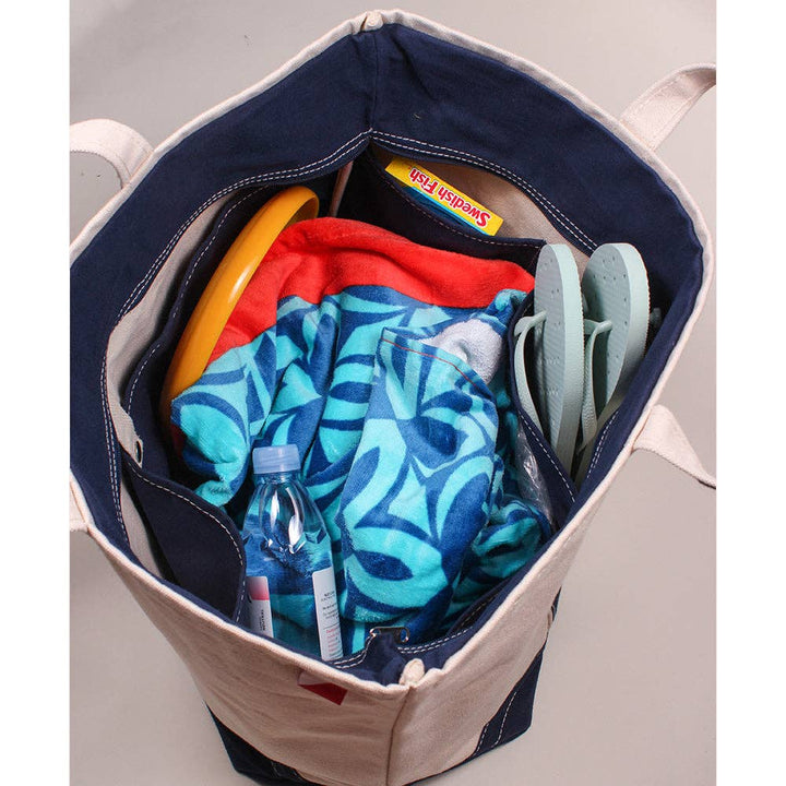 Canvas tote bag with samples of what can go inside of it including two towels, flip-flops, Swedish Fish candies, Frisbee, and a bottle of water.