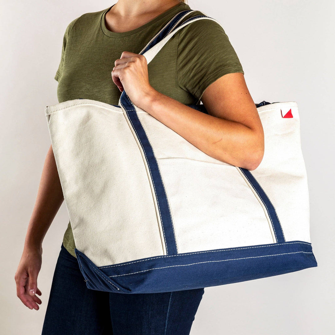 Person holding a canvas tote bag with dark blue handles and bottom panel.