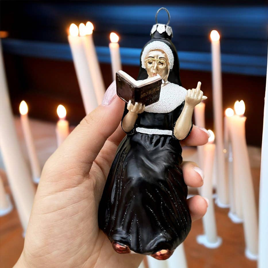 Decorative ornament of a nun holding a book, held in front of lit candles.