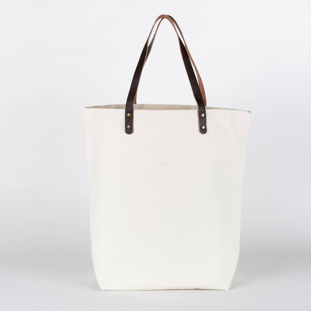 White tote bag with brown leather handles on a white background