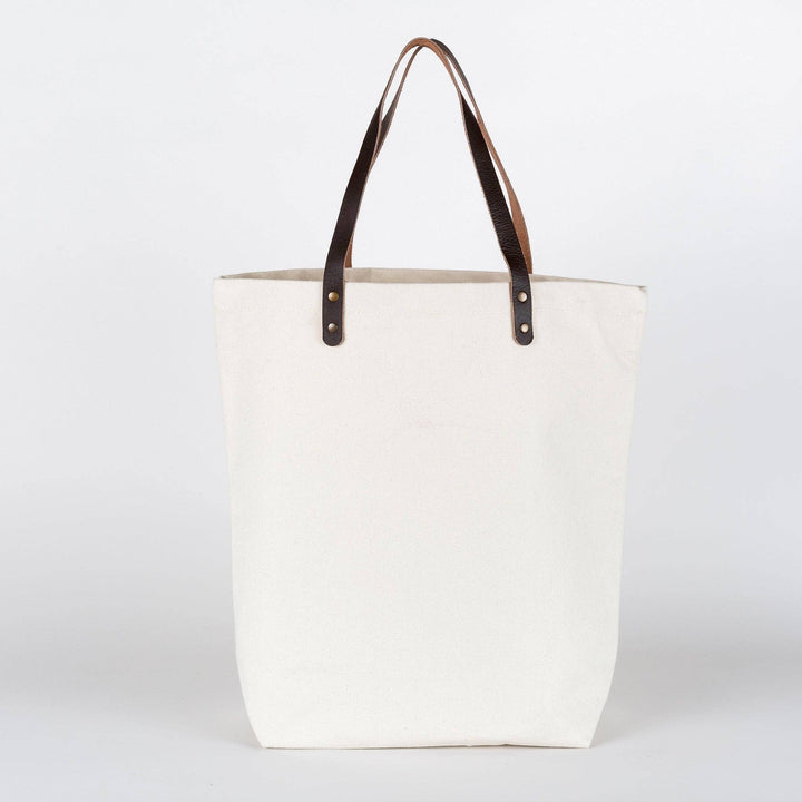 White tote bag with brown leather handles on a white background