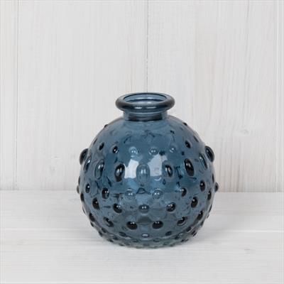 Blue textured vase on a white surface with a light wooden panel background