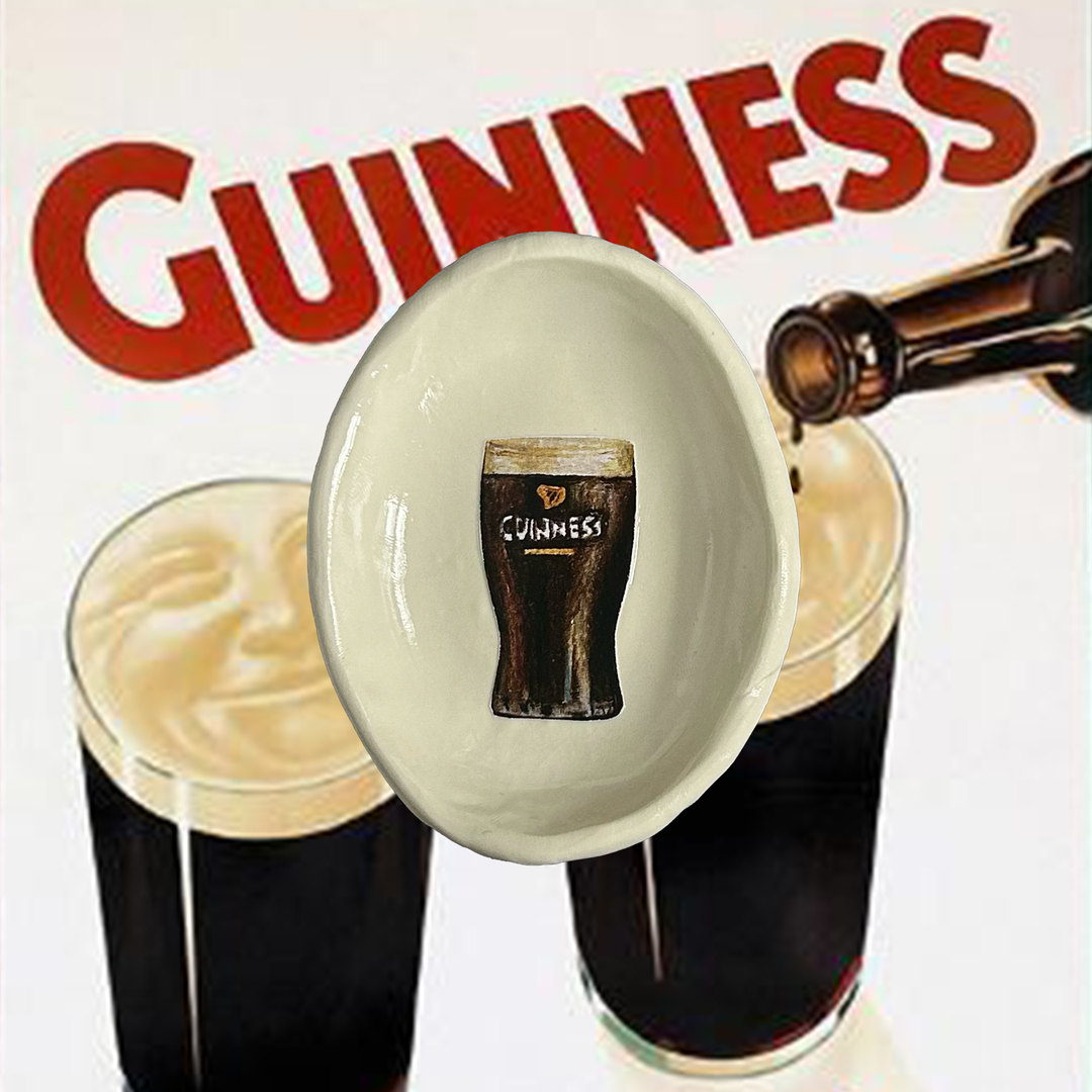 Handmade trinket dish with an illustration of Guinness and the tray is resting on a Guinness advertisement with a glass of Guinness being poured and the brand name displayed.