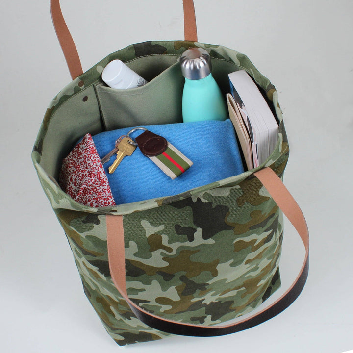 Camouflage tote bag with various items on a white background