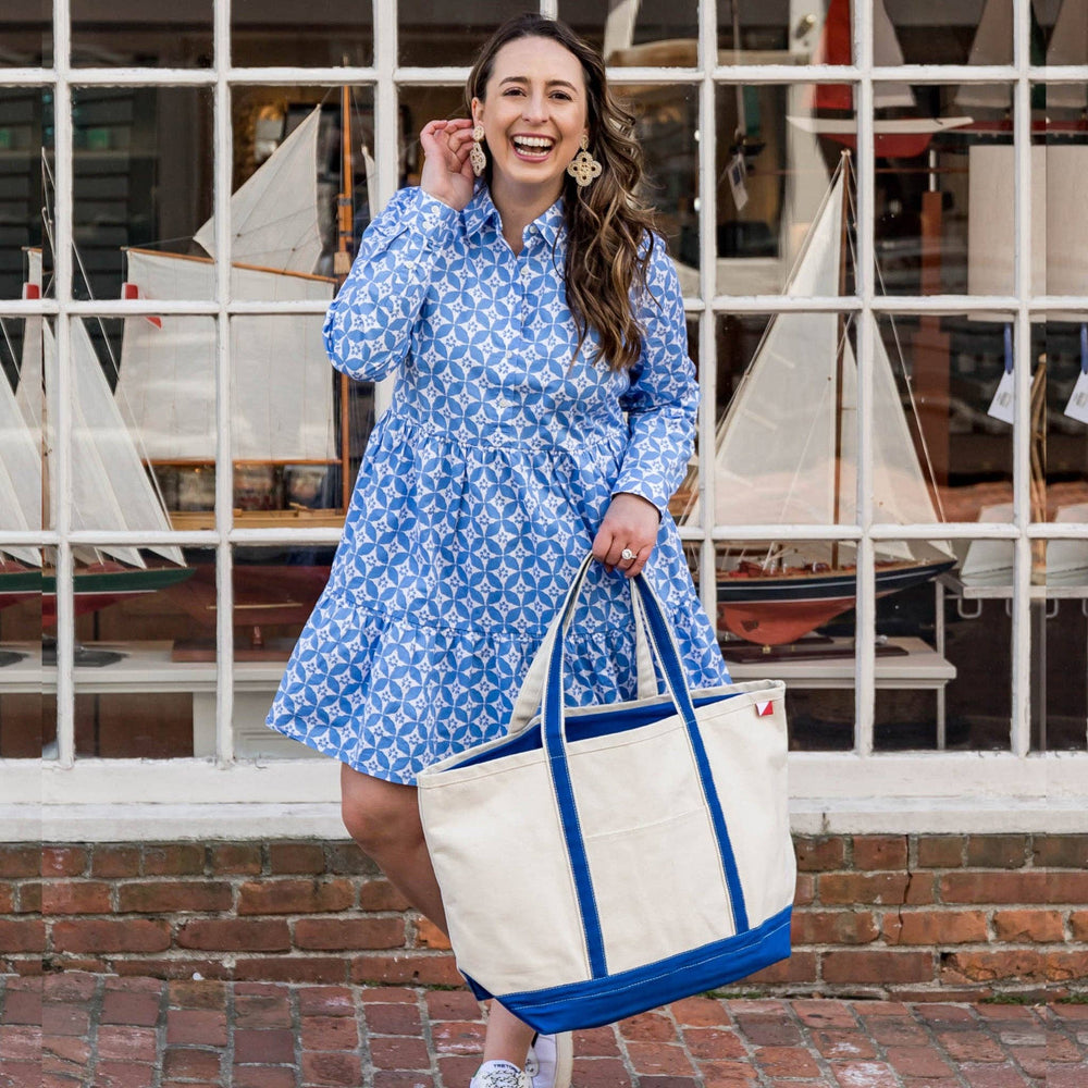 Woman in a blue dress holding a white tote bag with blue accents, standing in front of model sailboats.