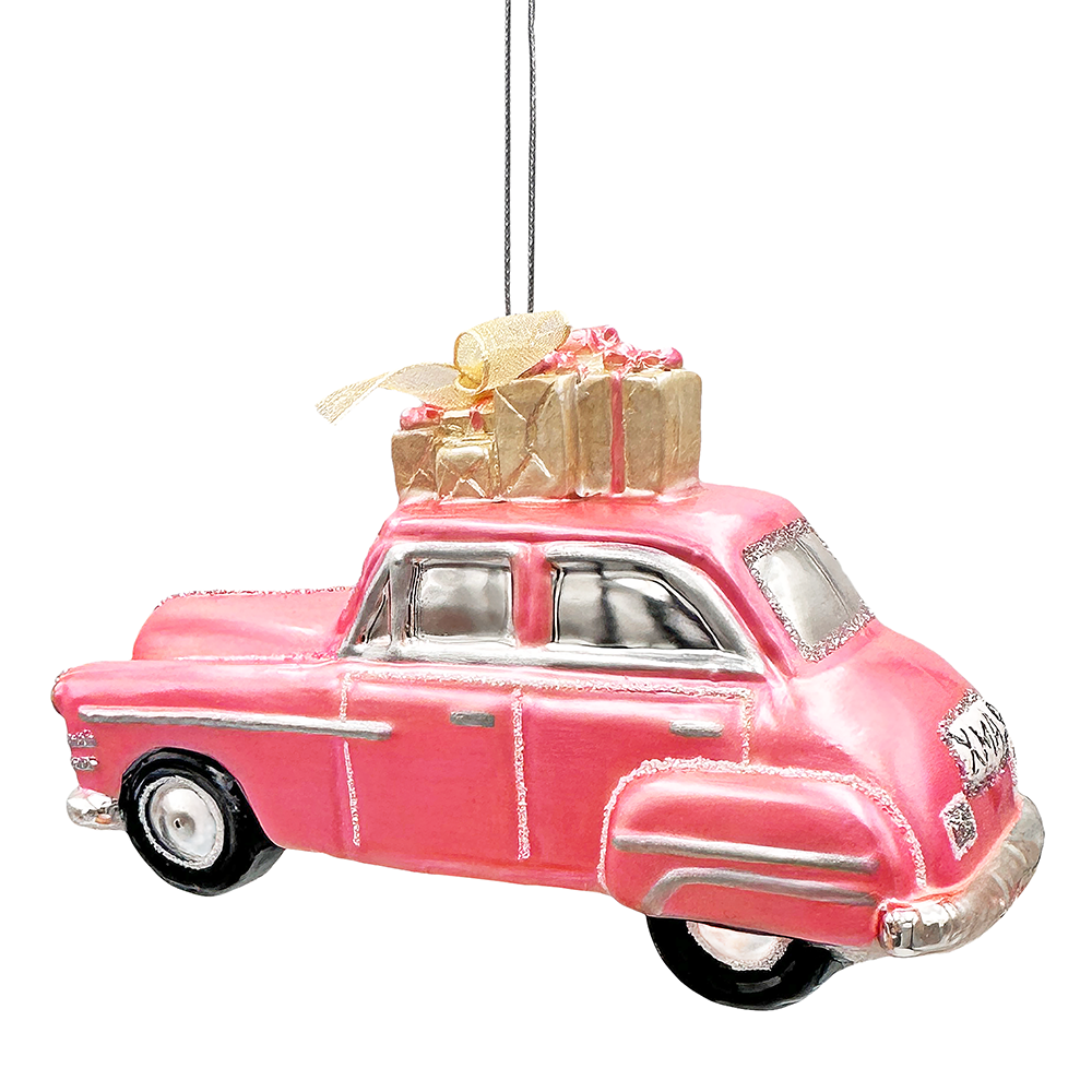 A pink vintage car Christmas ornament with silver trim, black wheels, and a gold gift box on its roof, hanging against a plain white background.