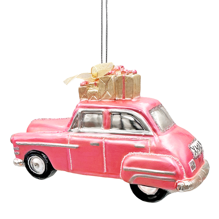 A pink vintage car Christmas ornament with silver trim, black wheels, and a gold gift box on its roof, hanging against a plain white background.