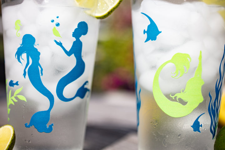 Both sides of the pretty pint glass with mermaids swimming and floating about
